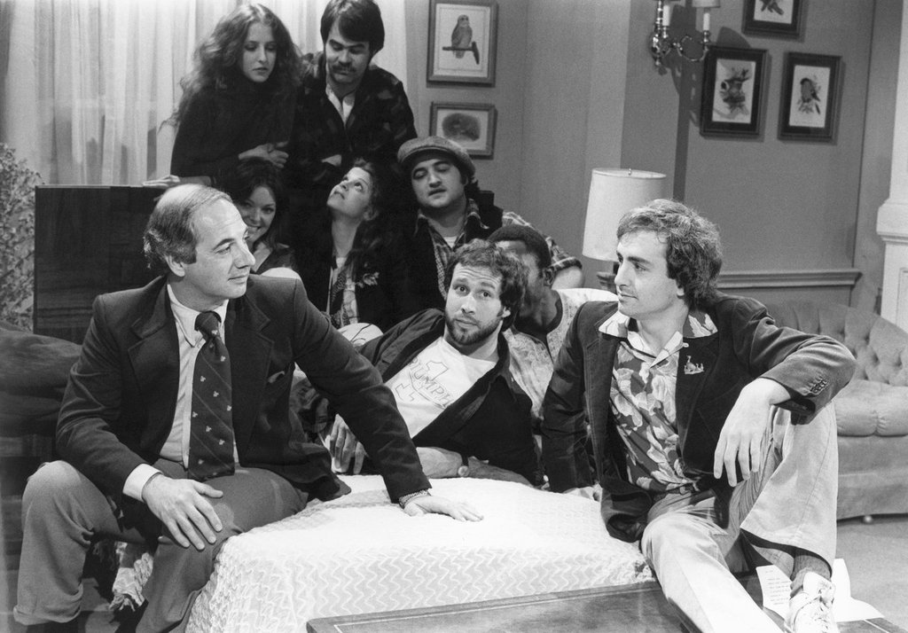 FILE - White House Press Secretary Ron Nessen, left, appears on the "Saturday Night Live" set with producer Lorne Michaels, right, and cast members Chevy Chase, foreground center, Laraine Newman, background left, Dan Aykroyd, background right, Jane Curtin, second row from left, Gilda Radner, John Belushi and Garret Morris, partially obscured, on April 17, 1976, in New York.