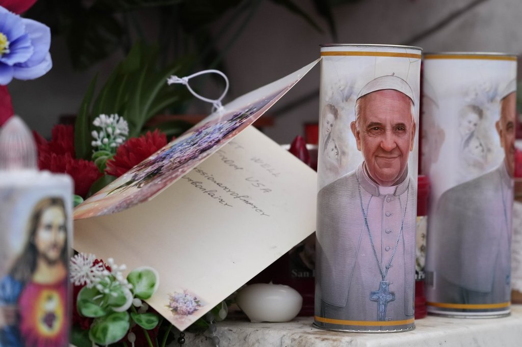 Candles with the pictures of Pope Francis are the laid under the statue of late Pope John Paul II outside Agostino Gemelli Polyclinic in Rome, Wednesday, Feb. 19, 2025, where the Pontiff is hospitalized since Friday, Feb. 14.