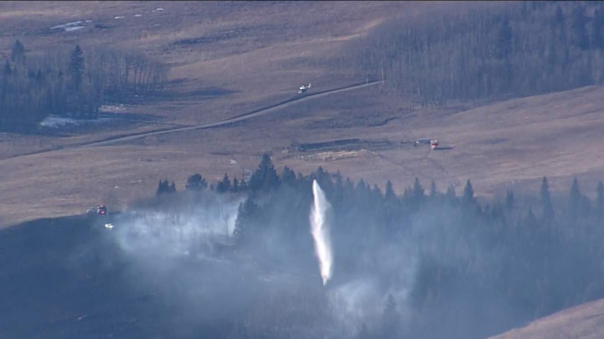 A helicopter with a water bucket helps fight a grass fire near Ghost Lake, west of Cochrane, Alta. on Tuesday, Feb. 25, 2025.