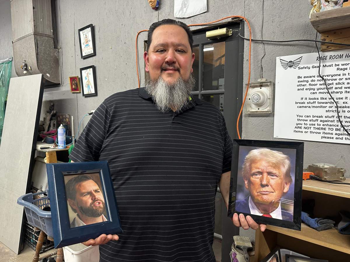 Terry LeBlanc, owner of the Rage Room Halifax, holds up Donald Trump and JD Vance framed photos.