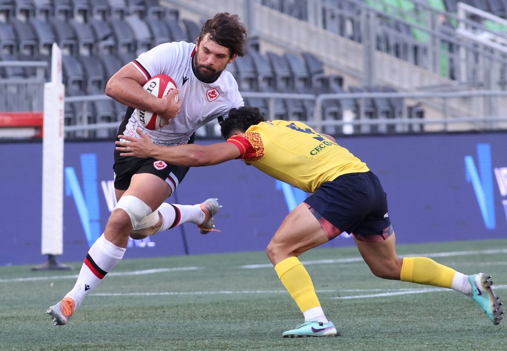 Canada's Lucas Rumball (8) runs with the ball as Romania's Alin Conache (9) tries to tackle him during the first half of men's rugby action in Ottawa on July 12, 2024.