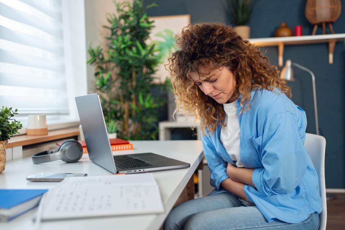 A woman experiences severe stomach pain while sitting at her desk. FluxFactory / Getty Images