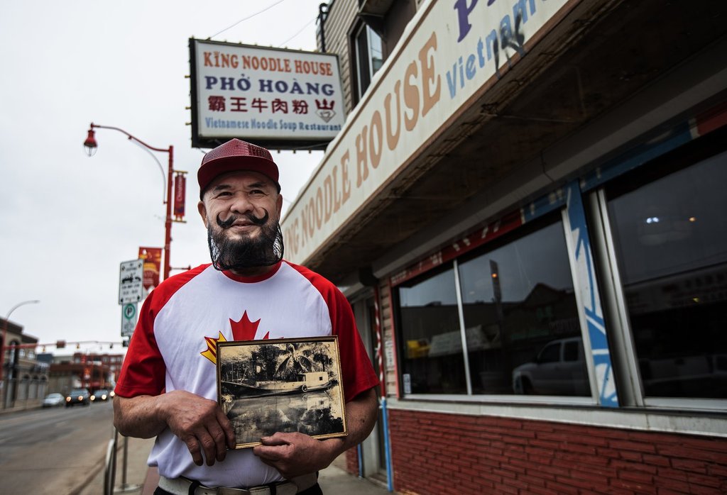 Tan Hoang stands outside his restaurant in Edmonton on Wednesday, April 16, 2025, holding a picture of the boat he built and used to escape Saigon after communists took over in 1975.