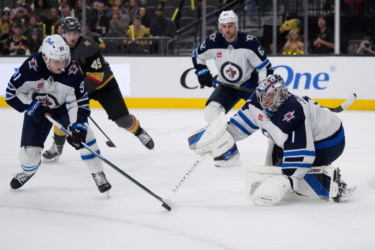 Winnipeg Jets goaltender Eric Comrie (1) knocks the puck to Winnipeg Jets center Cole Perfetti (91) during the second period of an NHL hockey game against the Vegas Golden Knights, Thursday, April 3, 2025, in Las Vegas. (AP Photo/John Locher).