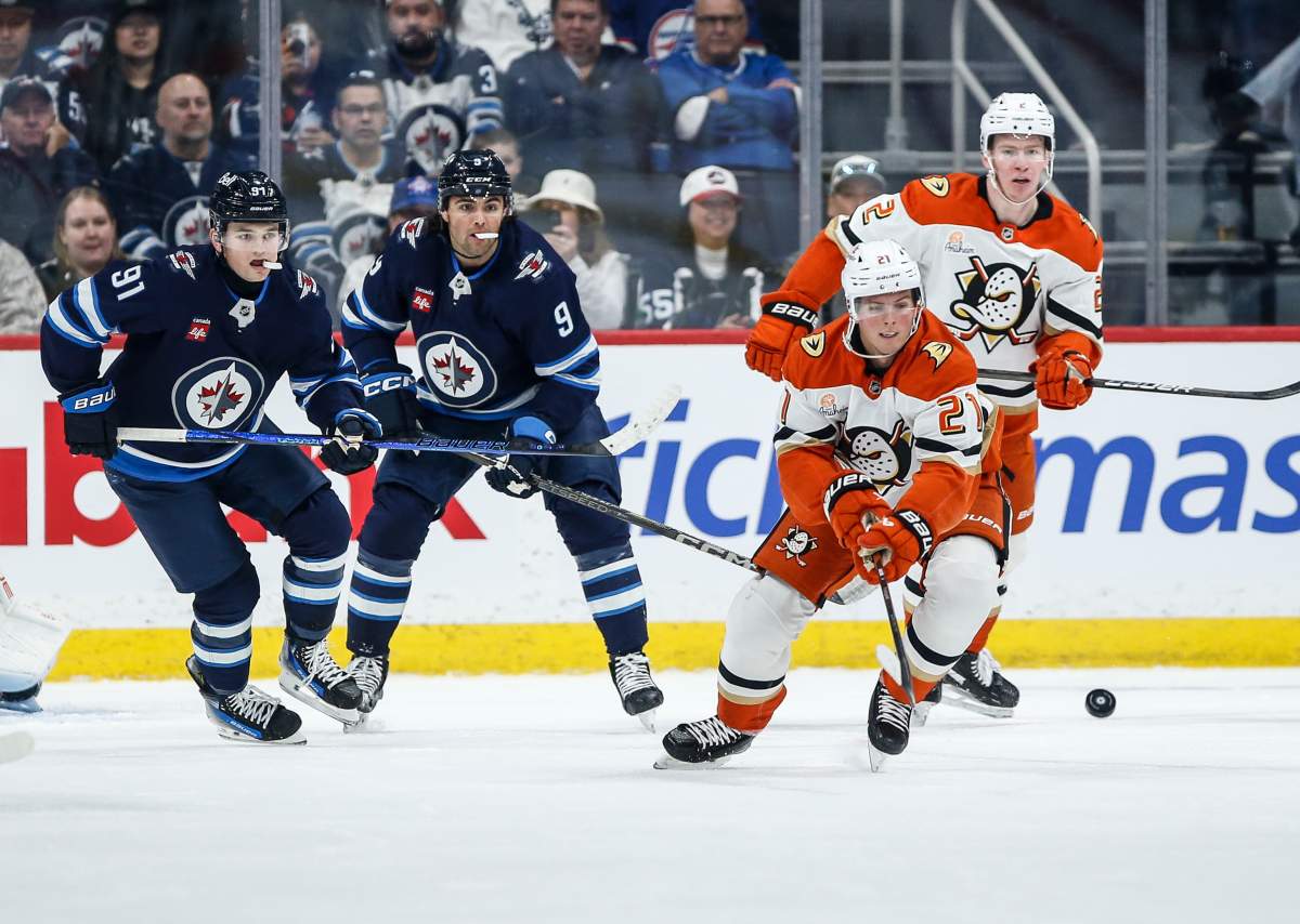Anaheim Ducks' Isac Lundestrom (21) clears the puck as Winnipeg Jets' Cole Perfetti (91) and Alex Iafallo (9) look on during first period NHL action in Winnipeg on Wednesday, April 16, 2025. THE CANADIAN PRESS/John Woods.
