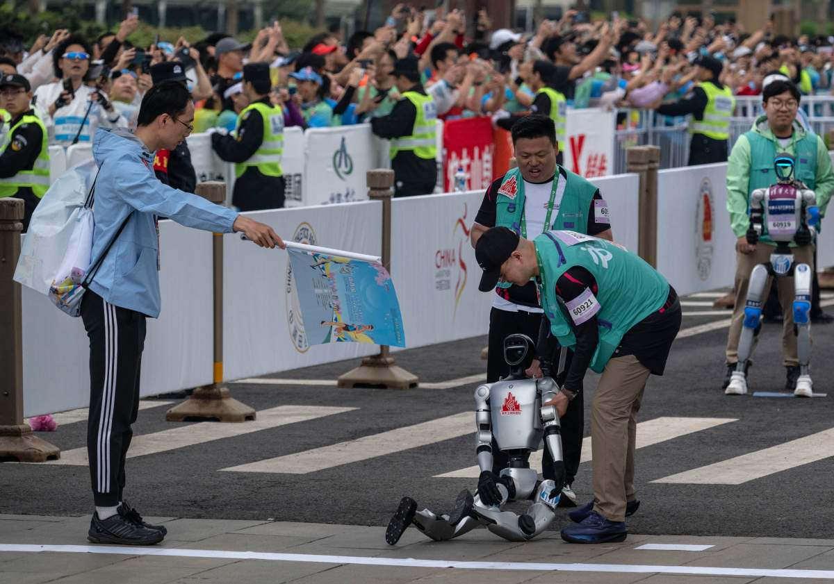 A humanoid robot is assisted by support technicians after collapsing at the start line of the Beijing E-Town Humanoid Robot Half Marathon on April 19, 2025 in Beijing, China. According to organizers, the event was the first of its kind and featured twenty-one humanoid robot runners.