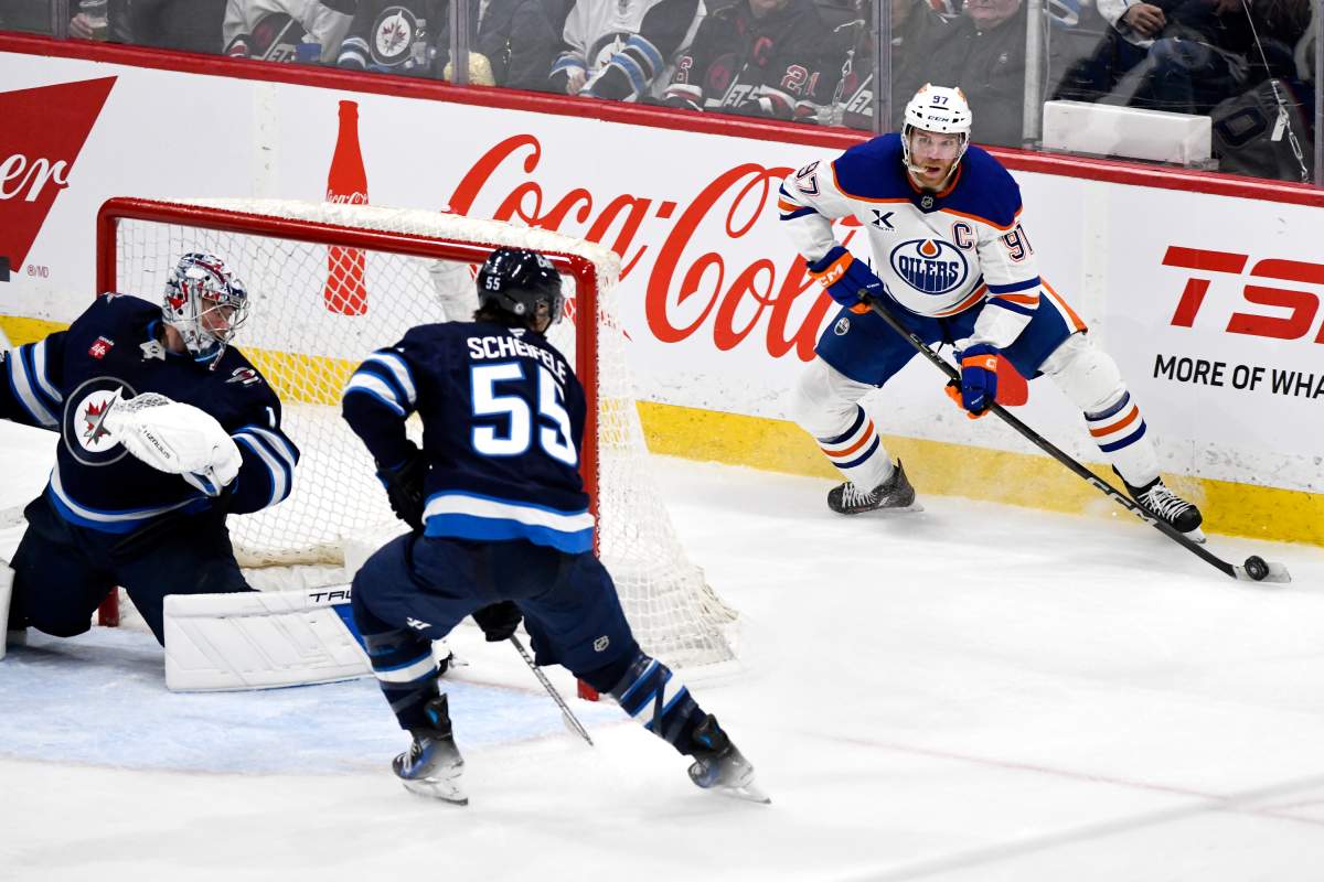 Edmonton Oilers' Connor McDavid (97) looks to make a pass around Winnipeg Jets' Mark Scheifele (55) and goaltender Eric Comrie (1) during third period NHL action in Winnipeg, Sunday April 13 2025.