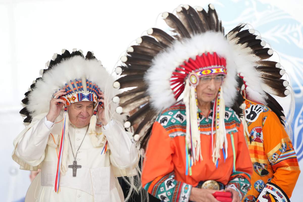 Pope Francis adjusts a traditional headdress he was given after his apology to Indigenous people as Chief Wilton Littlechild looks on during a ceremony in Maskwacis, Alta., as part of his papal visit across Canada on July 25, 2022.