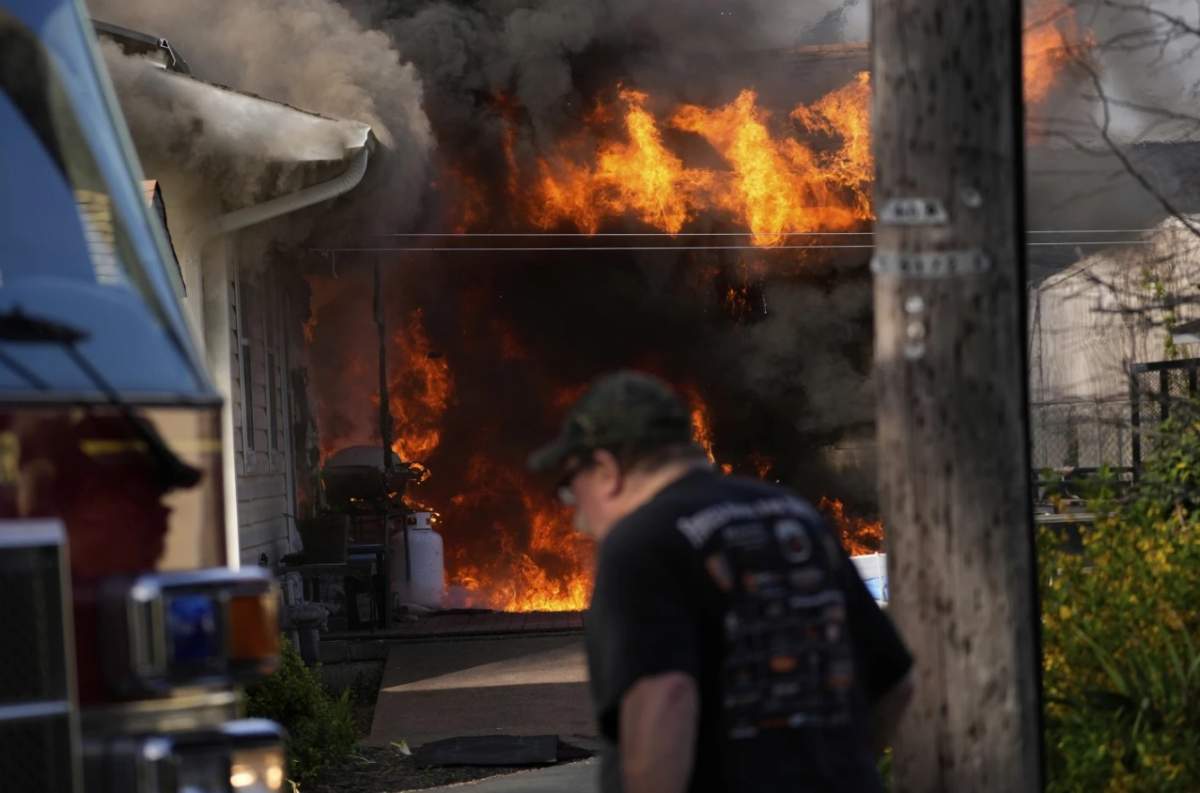 A man walks past a house fire Wednesday, April, 23,, 2025, in Lacey Township, N.J.