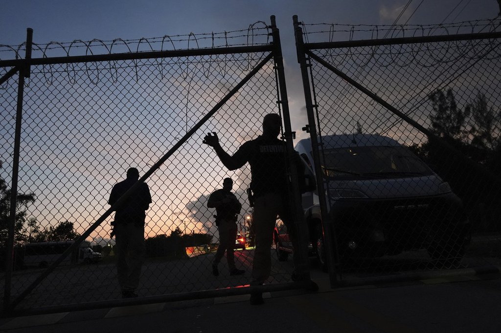 Krome Detention Center officers man an entrance gate as people hold a vigil outside to recognize those who have died in U.S. Immigration and Customs Enforcement custody, as well as those affected by mass deportations, Saturday, May 24, 2025, in Miami.