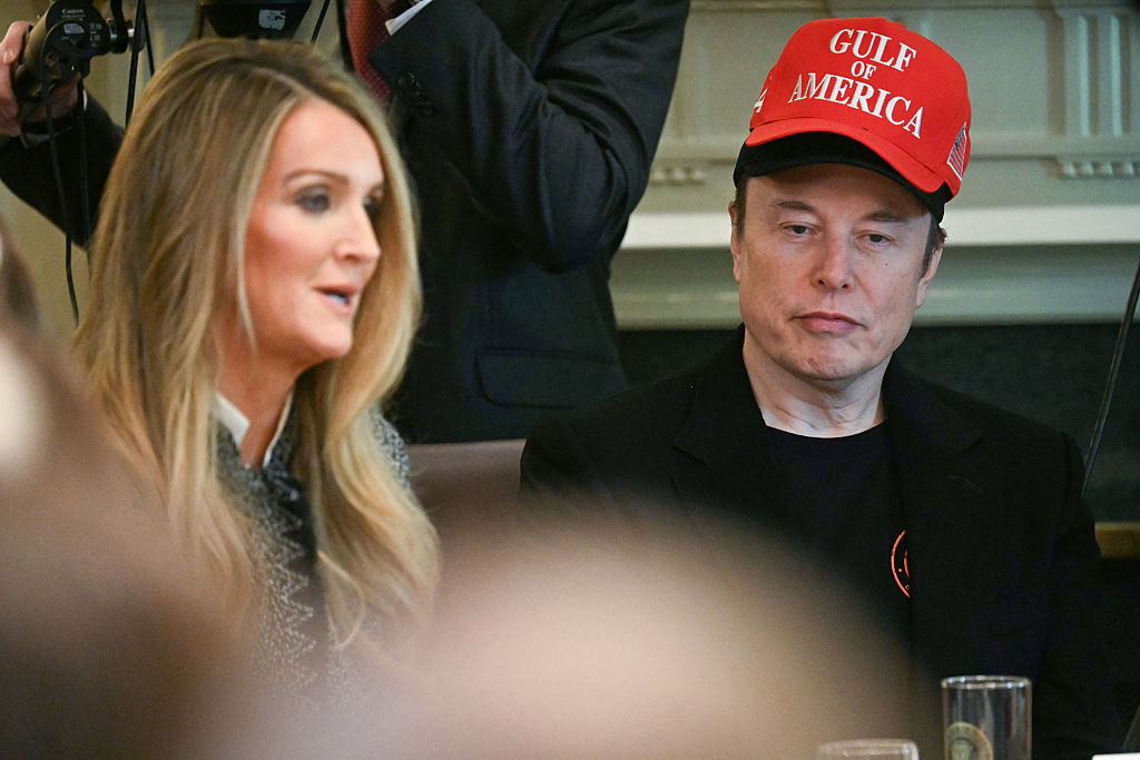 Elon Musk, wearing two hats, listens to US Administrator of the Small Business Administration Kelly Loeffler speak during a cabinet meeting in the Cabinet Room of the White House in Washington, DC, on April 30, 2025.