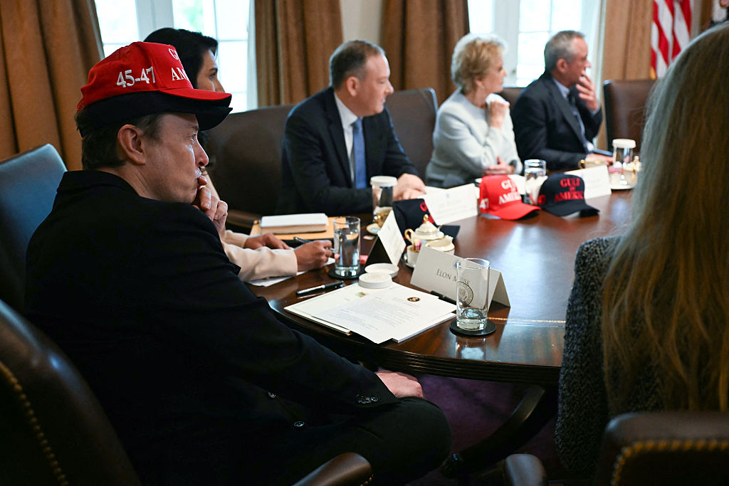Elon Musk, wearing two hats, looks on as US President Donald Trump holds a meeting with his Cabinet, in the Cabinet Room of the White House in Washington, DC, of April 30, 2025.