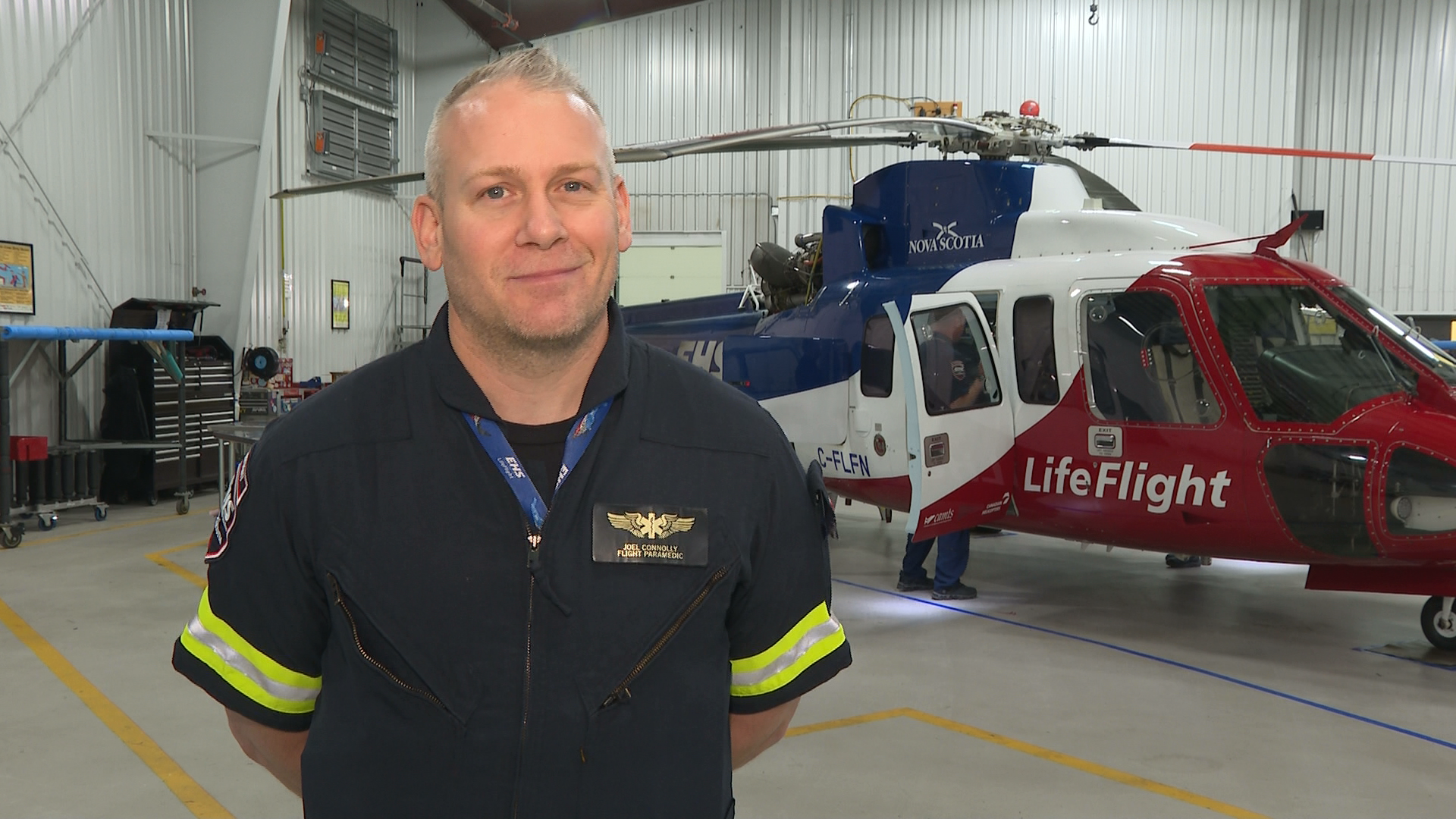 Joel Connolly is posing for his portrait in front of a red, blue and white LifeFlight helicopter.