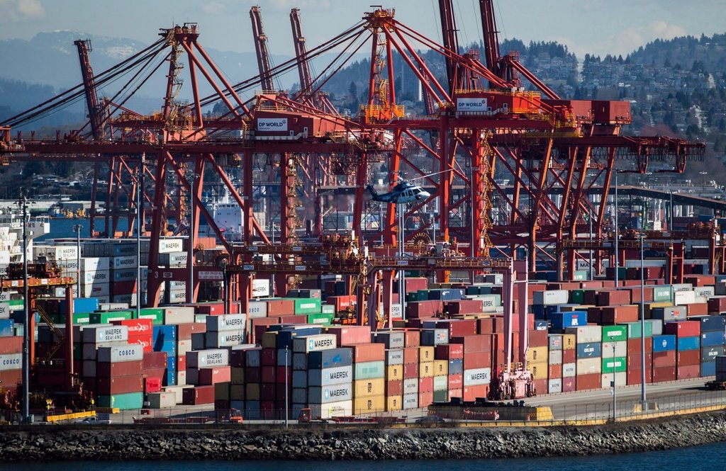 A Helijet helicopter preparing to land at the harbour passes by cranes used to load and unload container ships at the DP World marine terminal at Port Metro Vancouver, in Vancouver, B.C., on Friday March 16, 2018.