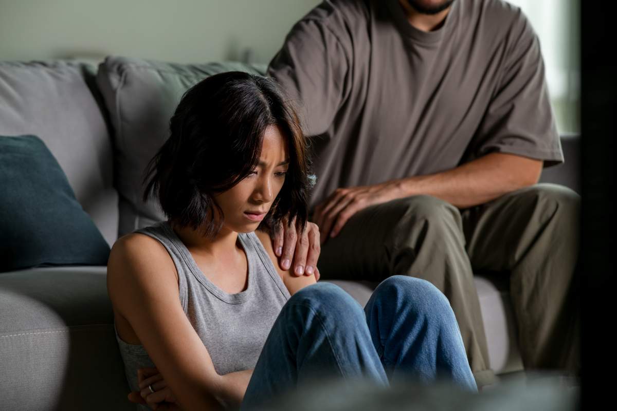 A man consoles his partner as she processes bad news from her insurance company.