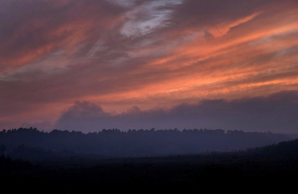 Smoke hangs above the treeline near dusk blocking out the setting sun at forest fires near Killarney, Ont.,  Tuesday, July 31, 2018. THE CANADIAN PRESS/Fred Thornhill.
