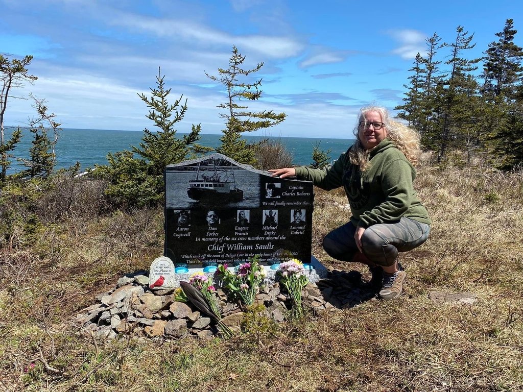 Lori Cogswell-Phillips crouches alongside a monument on Tuesday, May 10, 2022 in Delap's Cove, N.S. remembering her son Aaron Phillips and other members of the crew of the Chief William Saulis. She and a group of friends installed it near the site of where the boat sank on Dec. 15, 2020. THE CANADIAN PRESS/Lori Cogswell-Phillips.