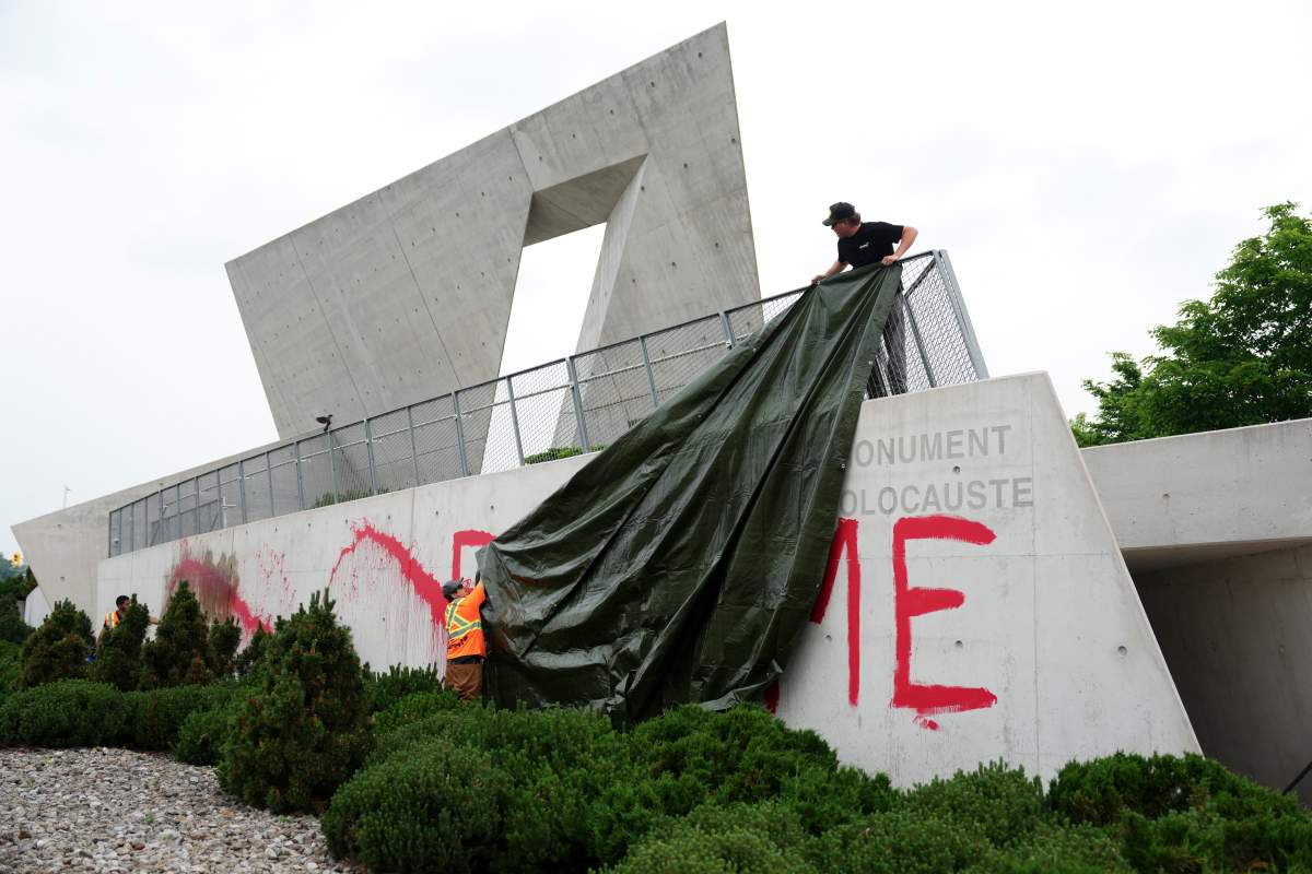 Workers from a cleanup crew spread a tarp to cover red paint spelling the words ‘FEED ME’ on the National Holocaust Monument in Ottawa on Monday, June 9, 2025. THE CANADIAN PRESS/Sean Kilpatrick