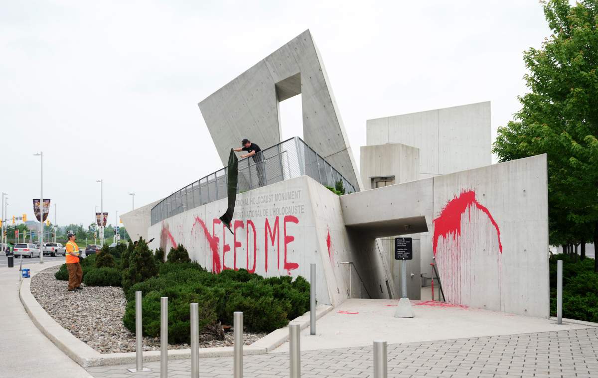 Workers from a cleanup crew spread a tarp to cover red paint spelling the words ‘FEED ME’ on the National Holocaust Monument in Ottawa on Monday, June 9, 2025. THE CANADIAN PRESS/Sean Kilpatrick