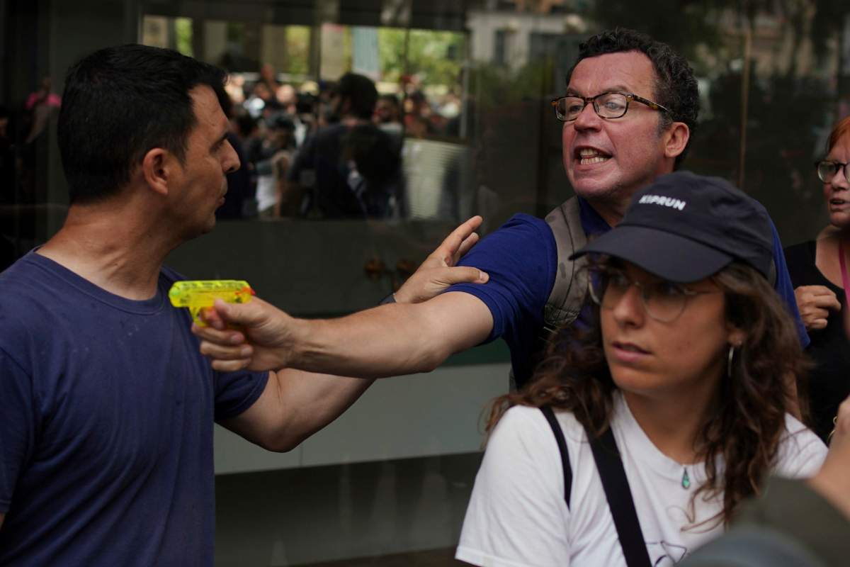 A plain clothed police officer, left, tries to stop a man shooting a water pistol during a protest against overtourism in Barcelona, Spain, Sunday, June 15, 2025. (AP Photo/Pau Venteo)