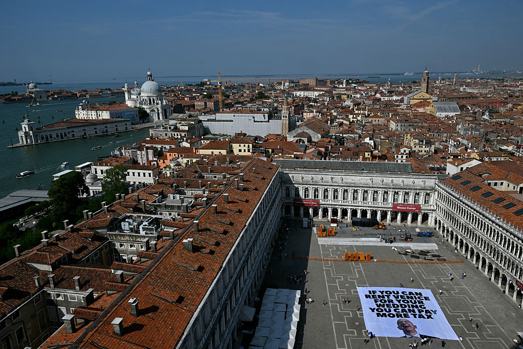 Activists of international environmental group Greenpeace deploy a giant banner displaying a picture of Jeff Bezos and reading "If you can rent Venice for your wedding you can pay more tax" at St. Mark Square in Venice on June 23, 2025.