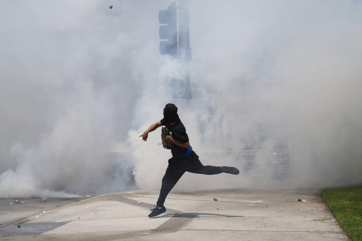 A protester throws a rock amidst tear gas from law enforcement during a demonstration after federal immigration authorities conducted operations, Saturday, June 7, 2025, in the Paramount section of Los Angeles.