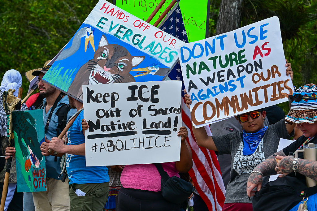 Demonstrators hold signs as they protest U.S. President Donald Trump's visit to a migrant detention center, dubbed "Alligator Alcatraz," located at the site of the Dade-Collier Training and Transition Airport in Ochopee, Florida on July 1, 2025.