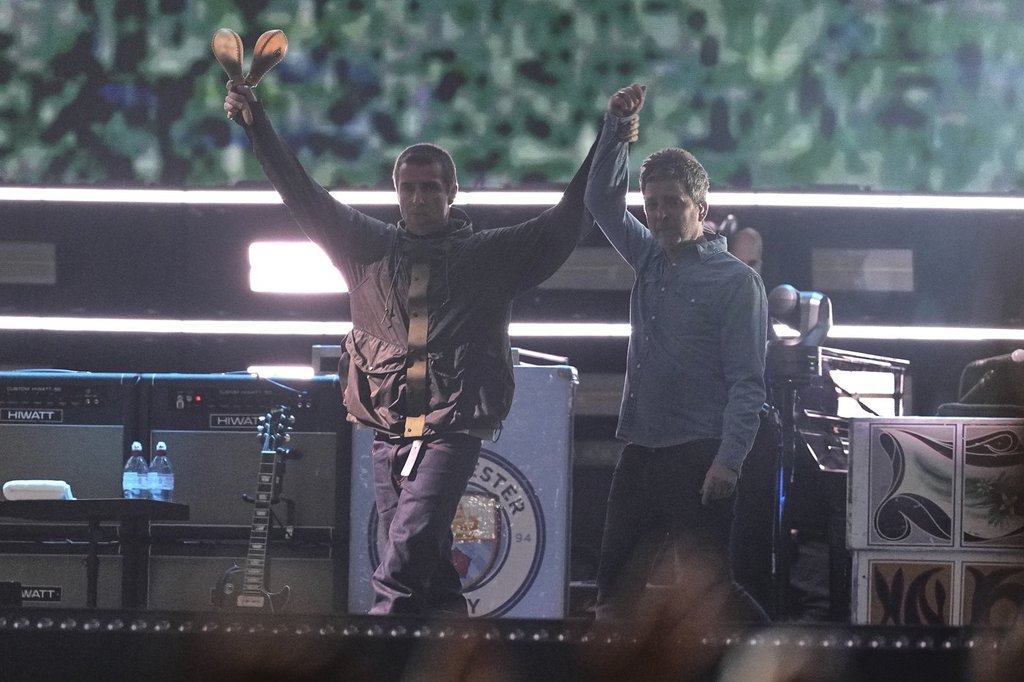 Liam Gallagher, left, holds the hand aloft of Noel Gallagher from the band Oasis as they perform during their reunion concert on Friday, July 4, 2025, in Cardiff.