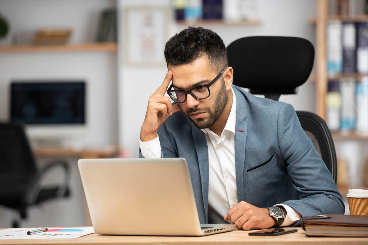 A businessman stares at his laptop with a confused look on his face.