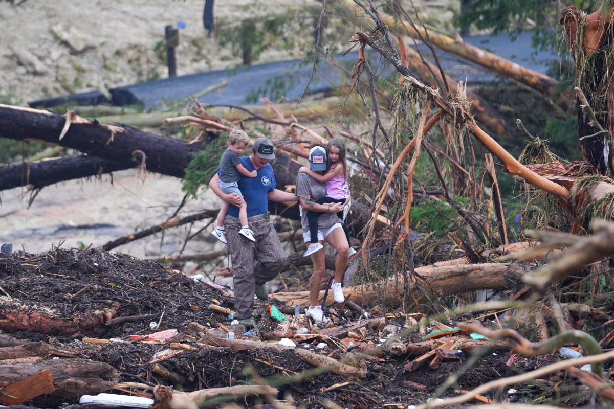 People climb over debris on a bridge atop the Guadalupe River after a flash flood swept through the area Saturday, July 5, 2025, in Ingram, Texas.