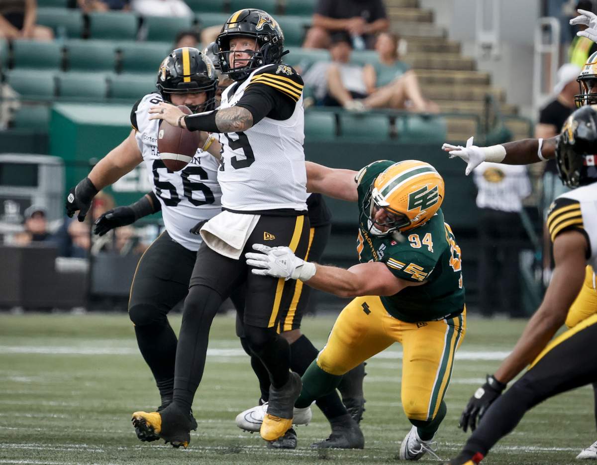 Hamilton Tiger-Cats quarterback Bo Levi Mitchell, centre, escapes the grasp of Edmonton Elks' Jake Ceresna during second half CFL football action in Edmonton, Saturday, Aug. 2, 2025.