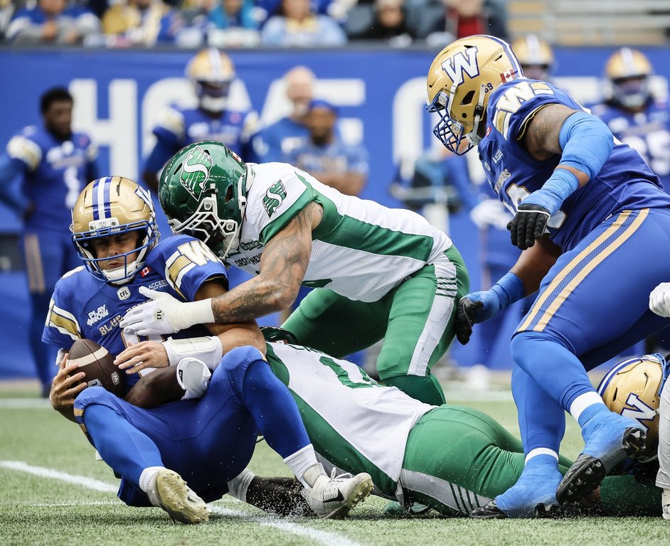 Winnipeg Blue Bombers quarterback Zach Collaros (8) gets sacked by Saskatchewan Roughriders' Malik Carney (11) and Shane Ray (5) during first half CFL action in Winnipeg, Saturday, Sept. 6, 2025. THE CANADIAN PRESS/John Woods.