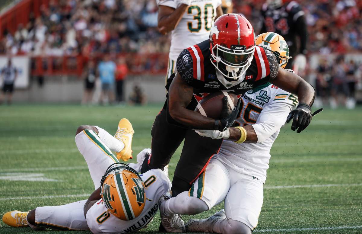 Edmonton Elks' Chelen Garnes, right, and Kobe Williams, left, tackle Calgary Stampeders' Dominique Rhymes during second half CFL football action in Calgary, Alta., Monday, Sept. 1, 2025.