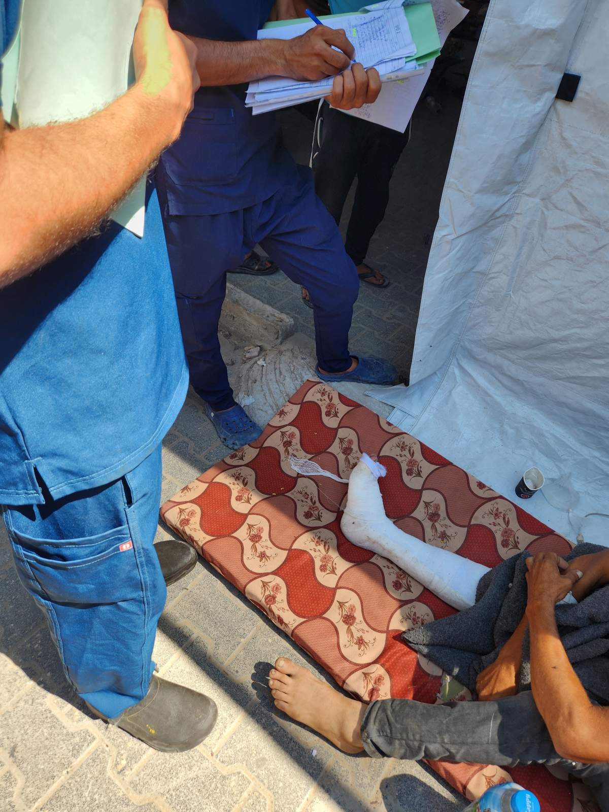 Doctors treating an injured man admitted to a mat on the floor beside a tent on July 25, 2025.