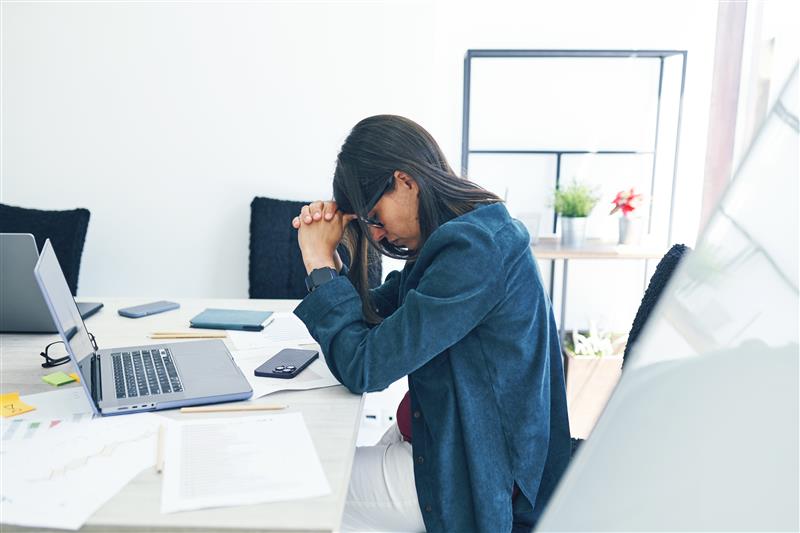 A businesswoman covers her face while sitting at her desk. Ekaterina Goncharova/Getty Images