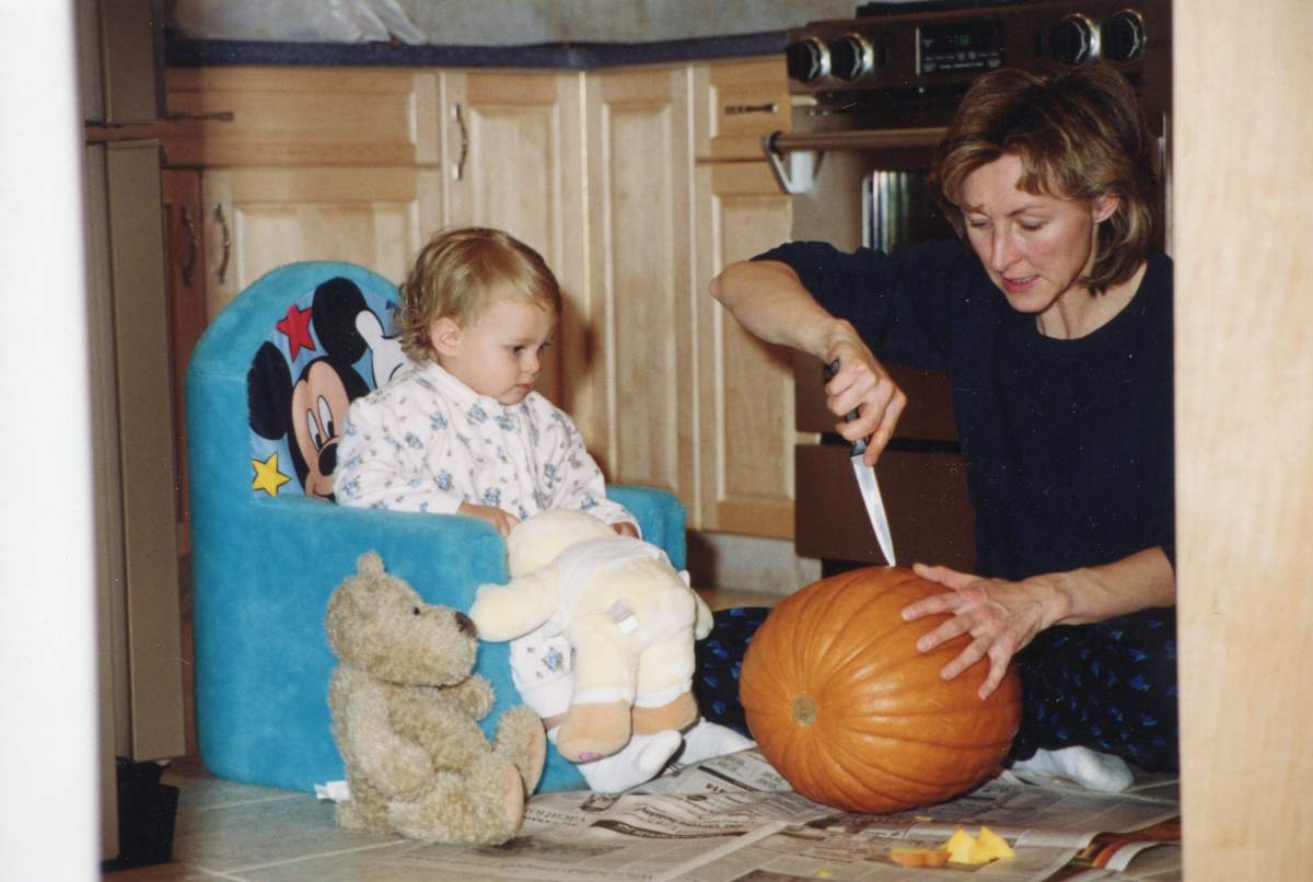 A woman carves a pumpkin with one of her daughters