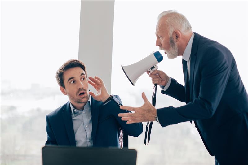 A manager stands over an employee and yells at the individual through a megaphone. RgStudio/Getty Images