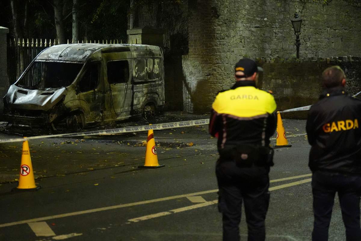 Garda Siochana police officers stand at the scene of a burned out police vehicle, near the Citywest Hotel, where disturbances have flared outside the Dublin hotel which used to house asylum seekers, Wednesday, Oct. 22, 2025. (Niall Carson/PA via AP).