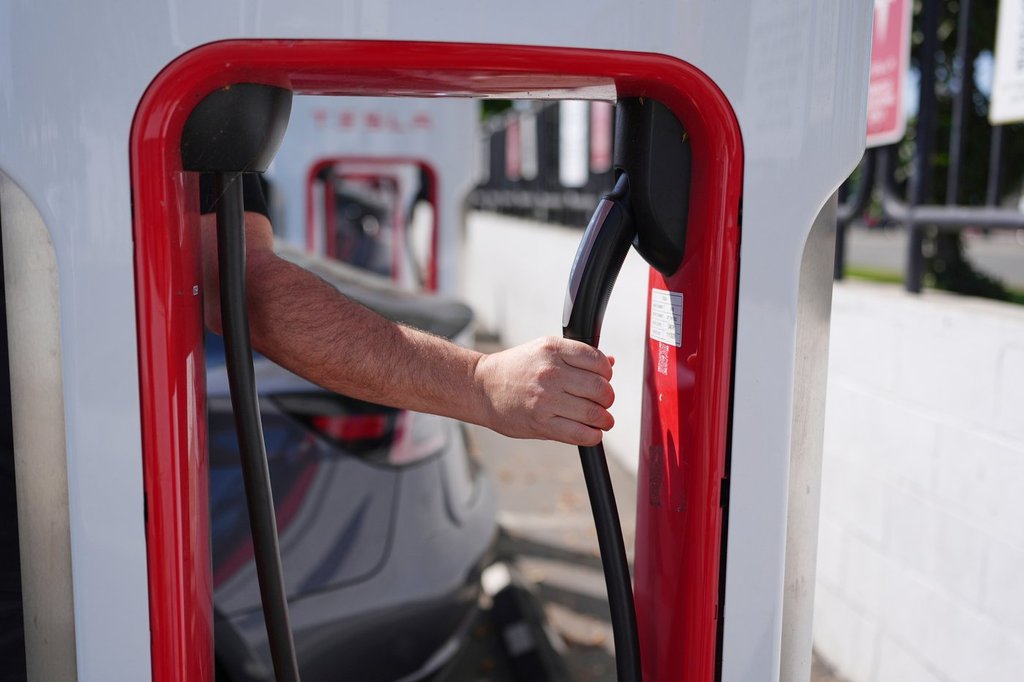 FILE - A person reaches to plug in an electric vehicle at a charging station May 22, 2025, in the City of Commerce, Calif. (AP Photo/Jae C. Hong, File).