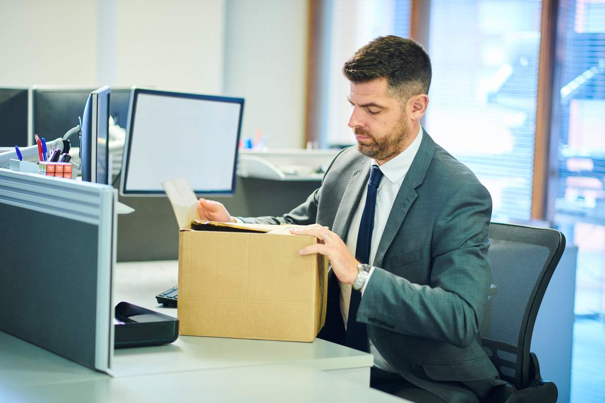 A businessman places office supplies in a cardboard box.