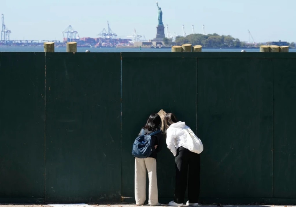 People look through fence to get a glance at the Statue of Liberty in New York, Wednesday, Oct. 1, 2025.
