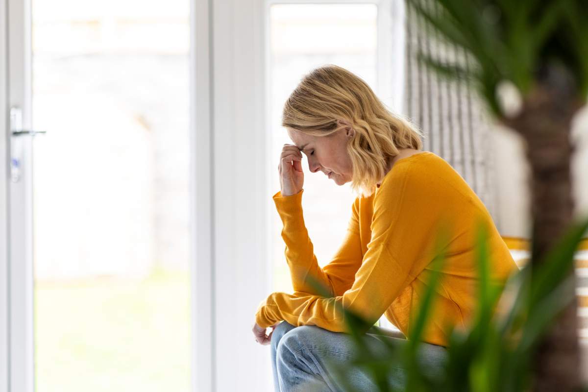 A woman rubs her forehead while sitting on a couch.