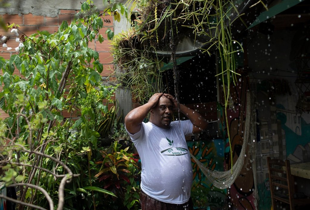 FILE - Luis Cassiano cools off with water that falls from his green roof at his home in Arara, a poor neighborhood, in Rio de Janeiro on Jan. 9, 2020. (AP Photo/Silvia Izquierdo, File).