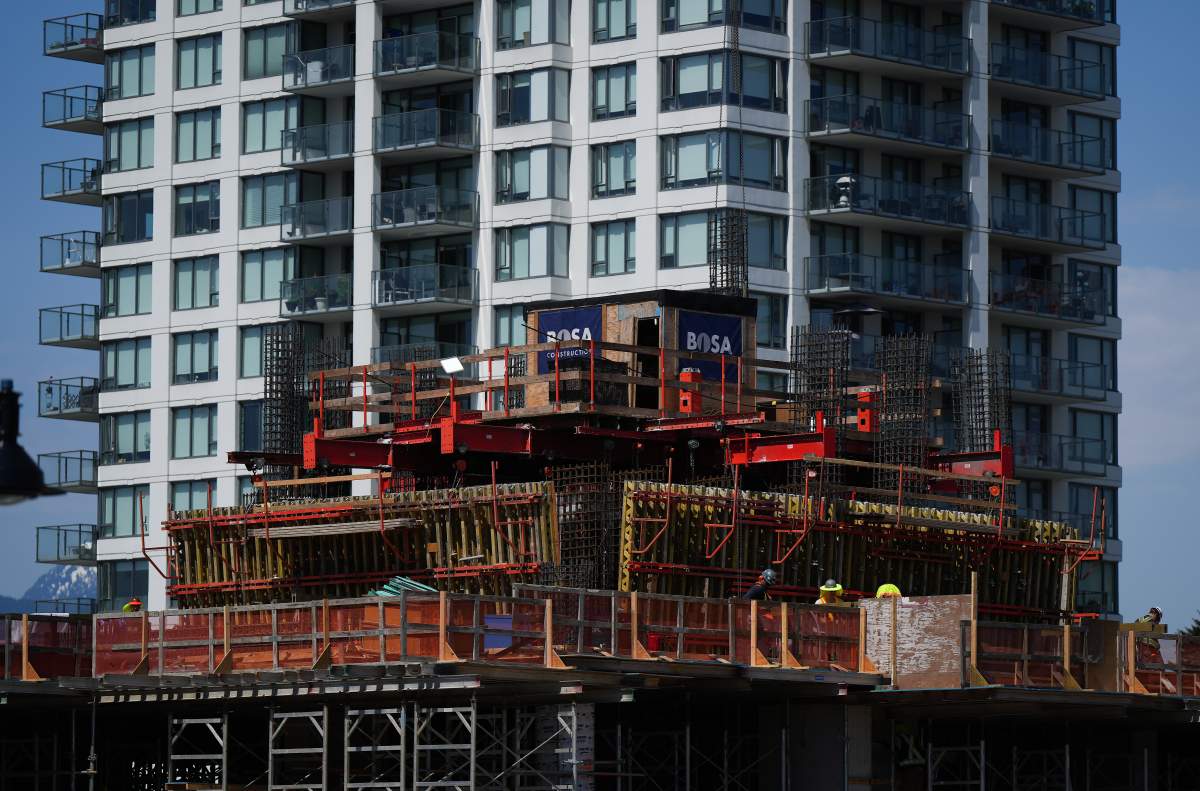 Workers are seen on a condo tower under construction as a completed one towers behind it in Coquitlam, B.C., on Tuesday, May 16, 2023.