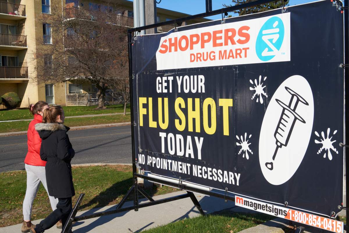 Women walk past a Shoppers Drug Mart sign promoting the flu shot, in Toronto on Nov. 14, 2020, amid the ongoing COVID-19 pandemic. 