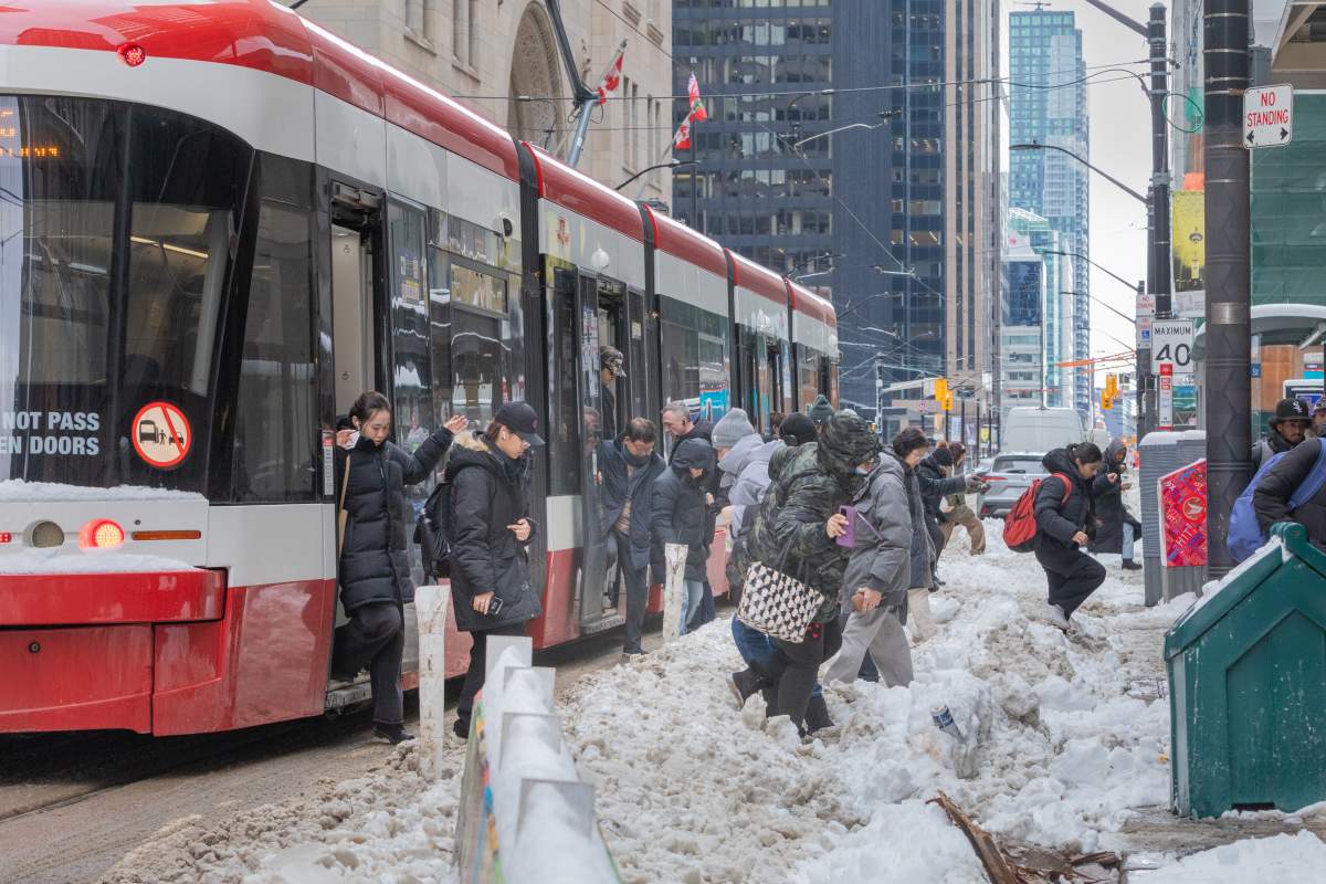 Streetcar riders clamber over a snowbank in downtown Toronto on Friday, Feb. 14, 2025.