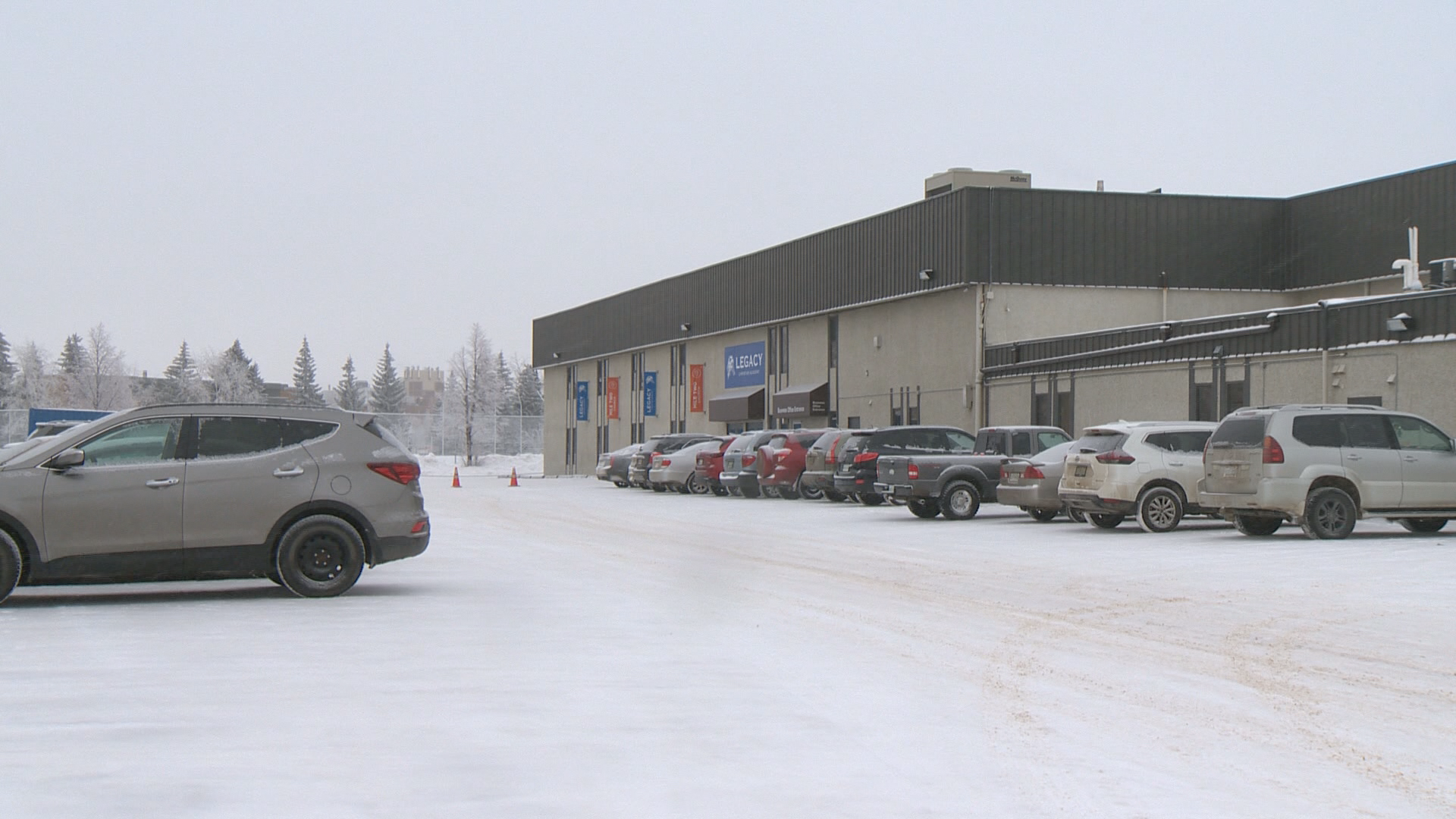 A beige and brown building is to the right of a parking lot covered in white snow.