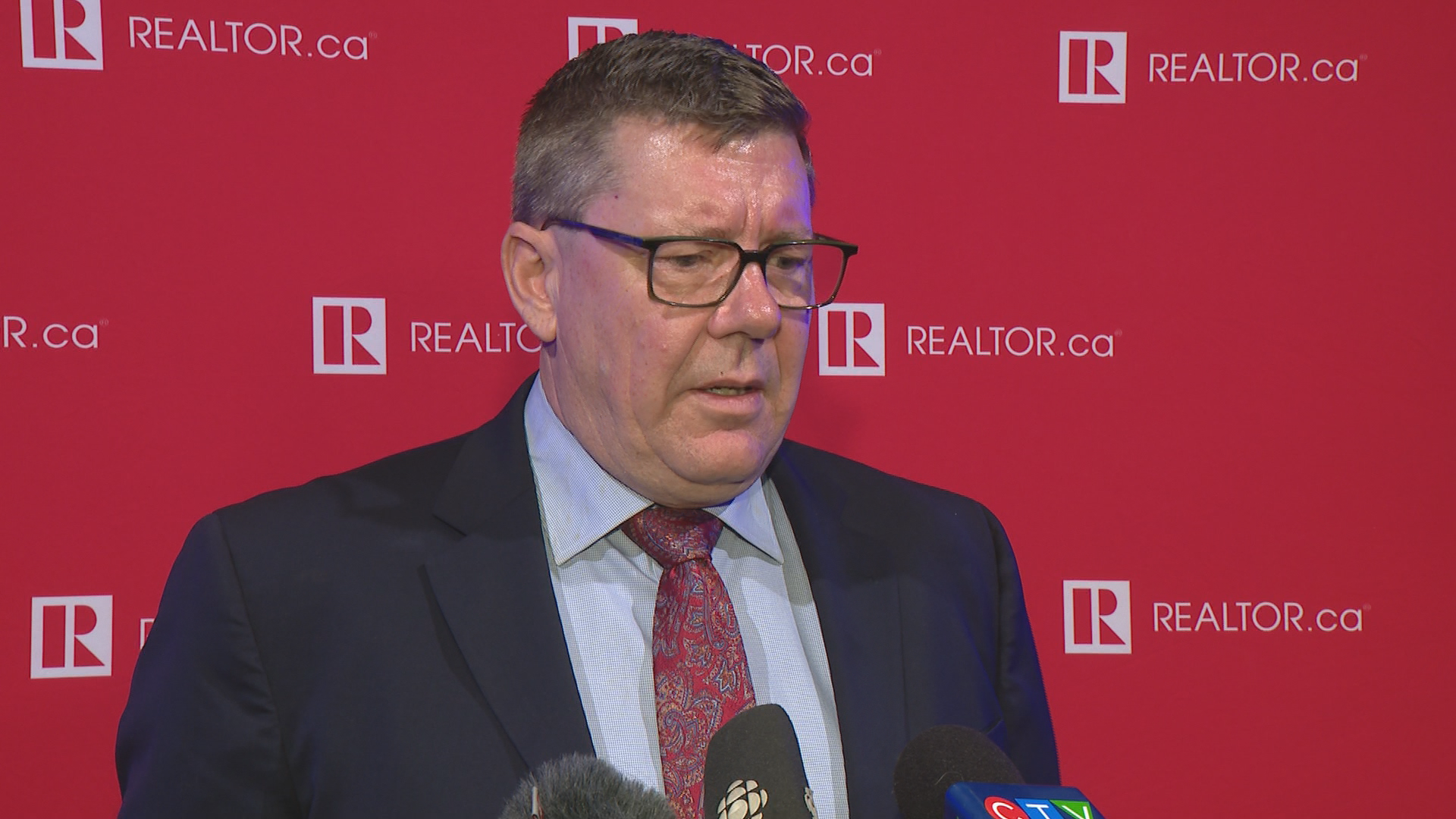 Premier Scott Moe stands in front of a red background.