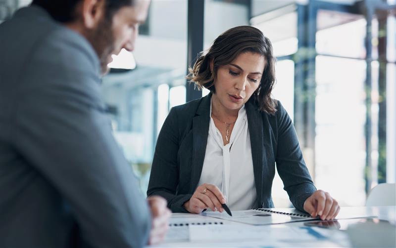 A professional reviewing employment documents with a colleague during a meeting, illustrating the process of seeking advice after a job loss or severance offer. shapecharge/Getty Images