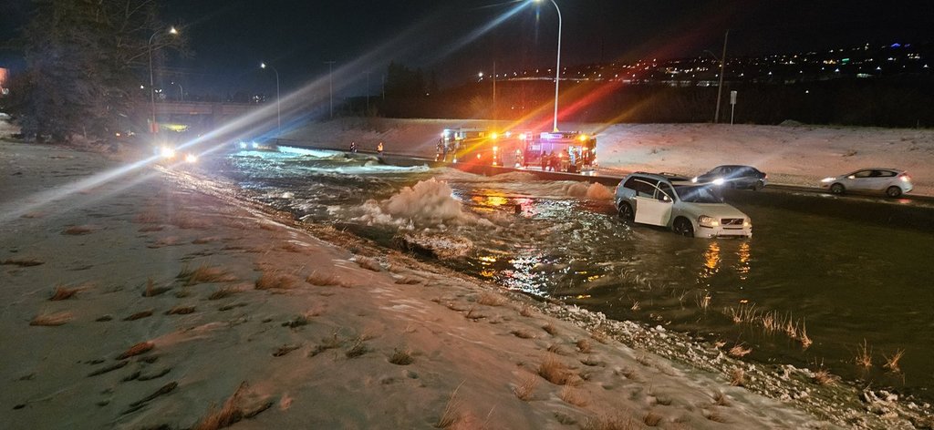 Firefighters stage at the side of a flooded highway as a broken water main, centre, near an abandoned car spews water onto the other lanes in Calgary, Alta., in a Tuesday, Dec. 30, 2025, handout photo. THE CANADIAN PRESS/Handout - Ian Royer (Mandatory Credit).